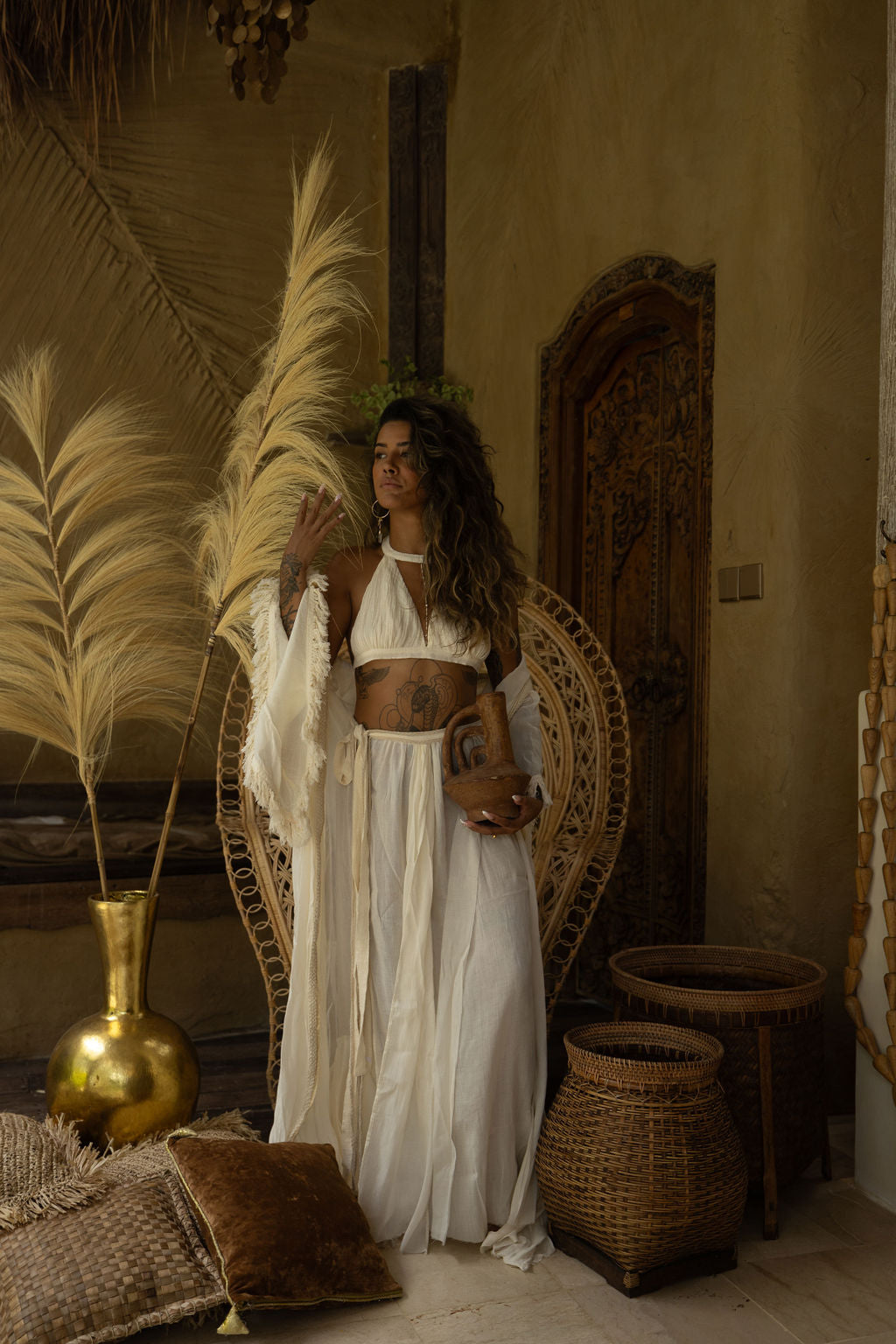 A model in the ivory Inika Set, seated in a serene, earthy-toned lounge adorned with natural decor. The soft, lightweight fabric drapes effortlessly, reflecting the essence of sustainable bohemian fashion. From Bird of Paradise, slow fashion Bali.
