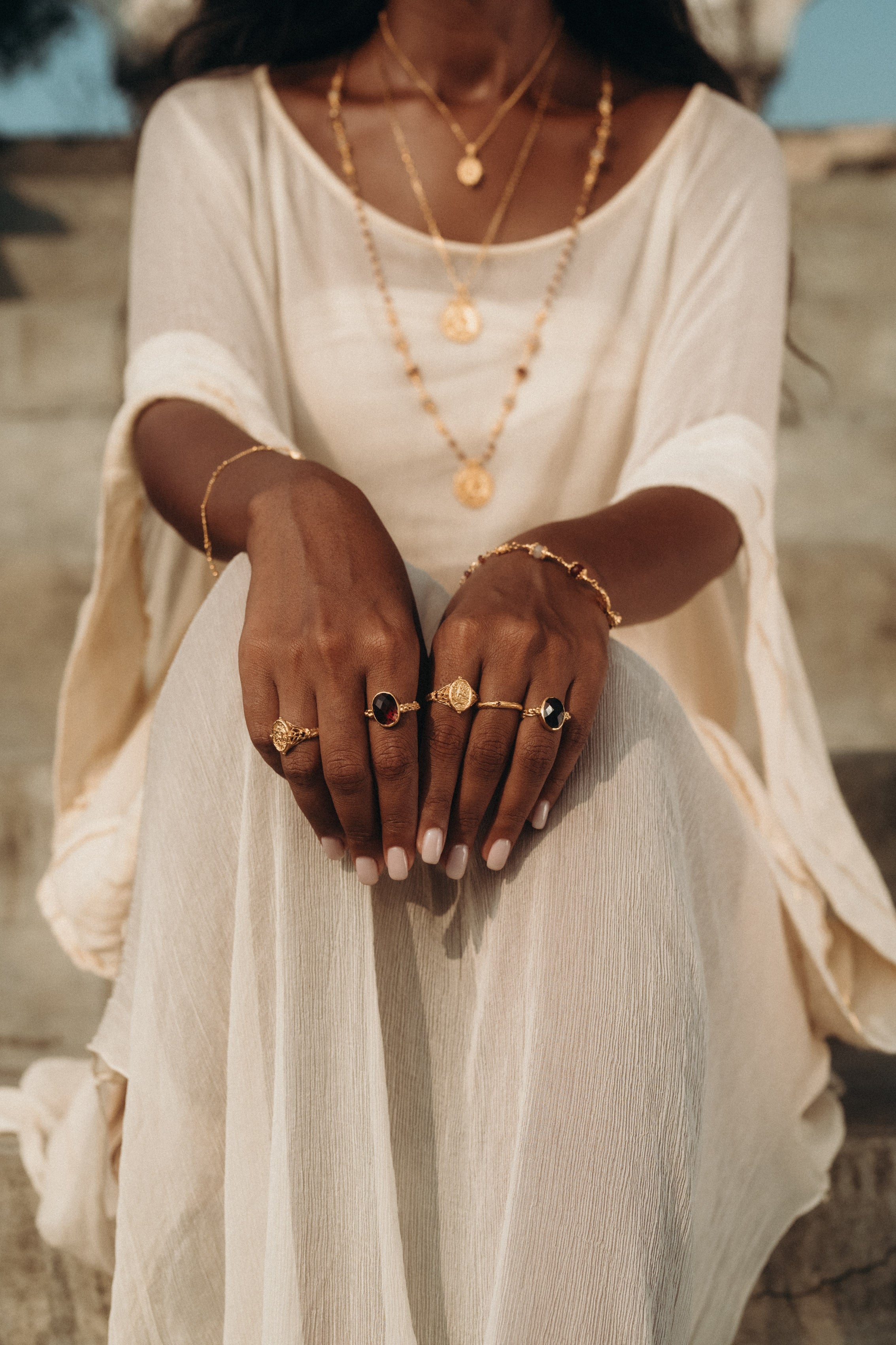 Close-up of a woman wearing handcrafted gold jewelry with gemstone rings and layered necklaces, paired with the Sundari Kaftan from Bird of Paradise. A perfect blend of bohemian elegance, luxury sustainable fashion, and mindful styling.