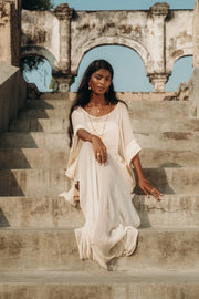 Woman sitting on stone steps wearing the Sundari Kaftan, a flowing sheer silk dress that embodies bohemian elegance and luxury sustainable fashion. Handcrafted in Bali, this slow fashion piece is perfect for mindful fashion lovers.
