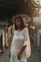 Woman in a sheer, flowing Sundari Kaftan from Bird of Paradise, made of natural silk chiffon, standing in golden sunset light. This luxury sustainable fashion piece embodies Bali boho clothing and slow fashion elegance.