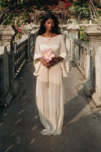 Woman standing gracefully in the Sundari Kaftan from Bird of Paradise, a sheer silk chiffon dress that embodies bohemian elegance and mindful fashion. Holding a pink lotus flower, she reflects the essence of Bali boho clothing and luxury sustainable fashion.