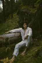 Kairos Pants worn with a linen shirt, seated against a fallen tree