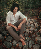 Man wearing the Udara handloom linen and cotton shirt, seated on river stones